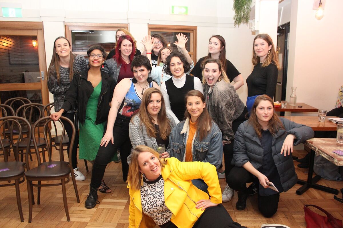 13 comedians posing together in a restaurant