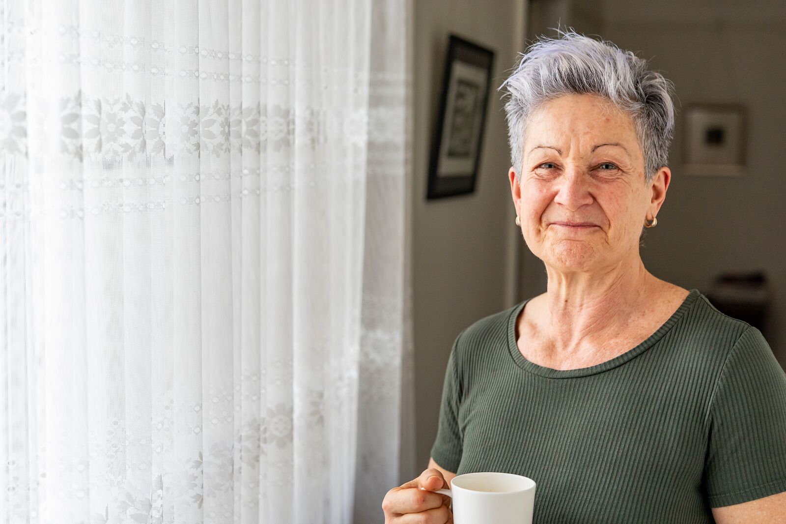 Elderly woman with a cup of tea standing by a window