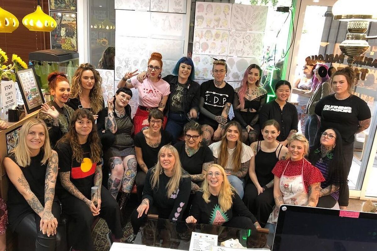 19 tattoo artists standing together smiling at the Not Just a Girl tattoo fundraising event