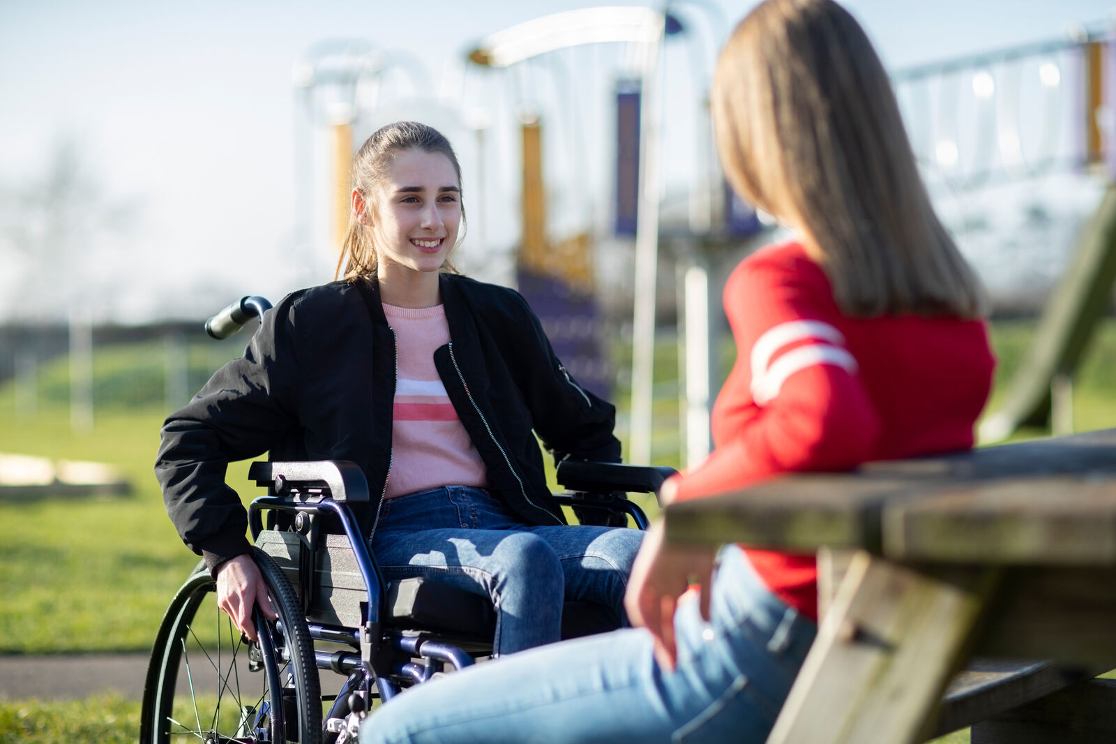 Young woman who uses a wheelchair talking to another young woman in a park