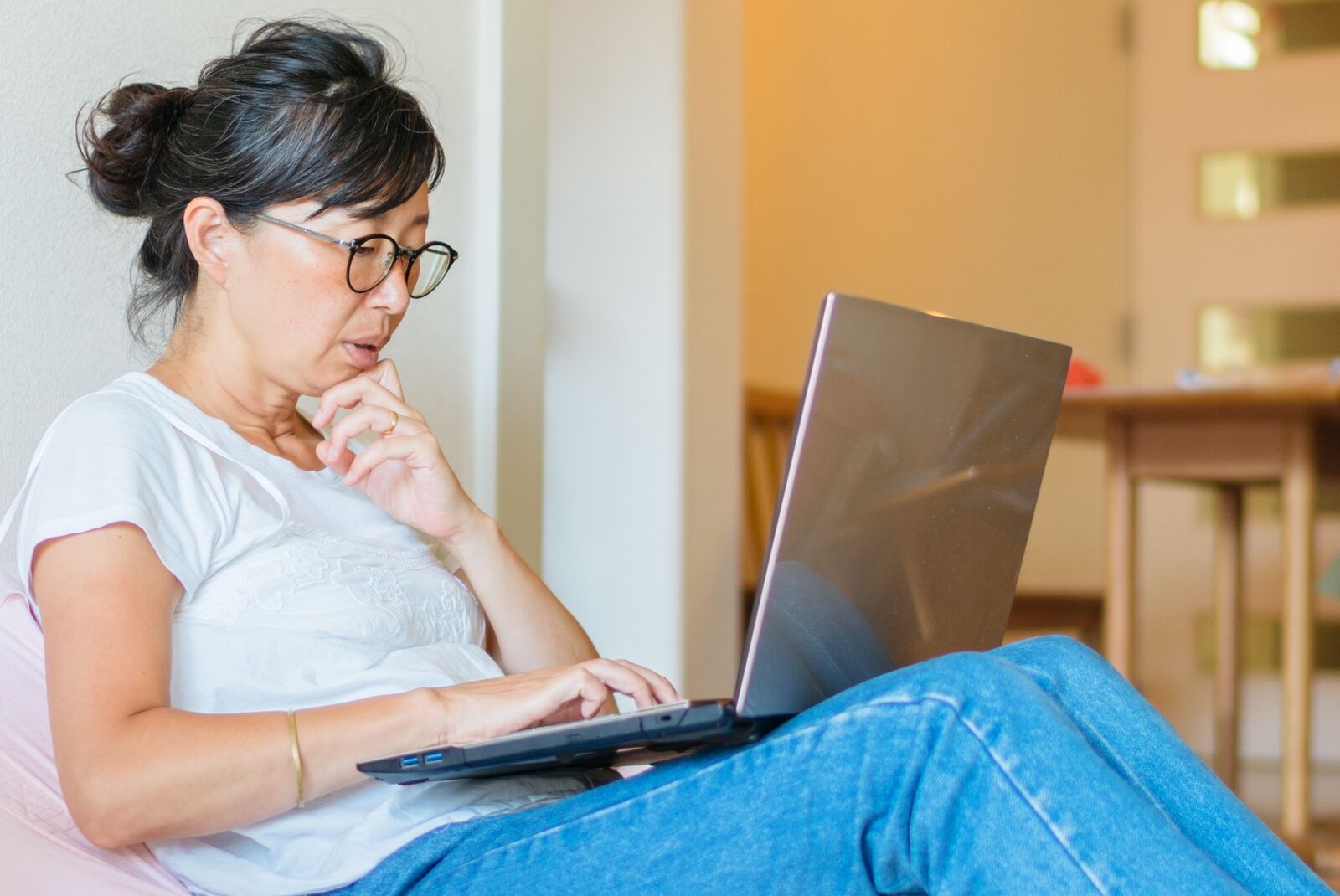 Asian woman in jeans and glasses woman looking at laptop